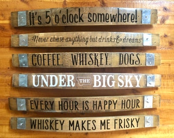 May include: Six wooden barrel stave signs with various sayings. The sayings are: "It's 5 o'clock somewhere!" "Never chase anything but drinks & dreams" "COFFEE. WHISKEY. DOGS." "UNDER THE BIG SKY" "EVERY HOUR IS HAPPY HOUR" "WHISKEY MAKES ME FRISKY"