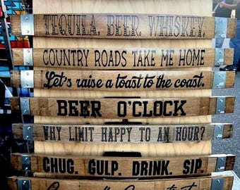 May include: A wooden display featuring several curved wooden planks with engraved text. The planks are held together with metal brackets. The text includes phrases like "TEQUILA. BEER. WHISKEY" and "COUNTRY ROADS TAKE ME HOME."