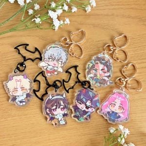 May include: Collection of acrylic keychains featuring anime-style characters. Each keychain has a unique character design with vibrant colors and attached to a gold-colored keyring. Some keychains have a black bat-shaped charm.