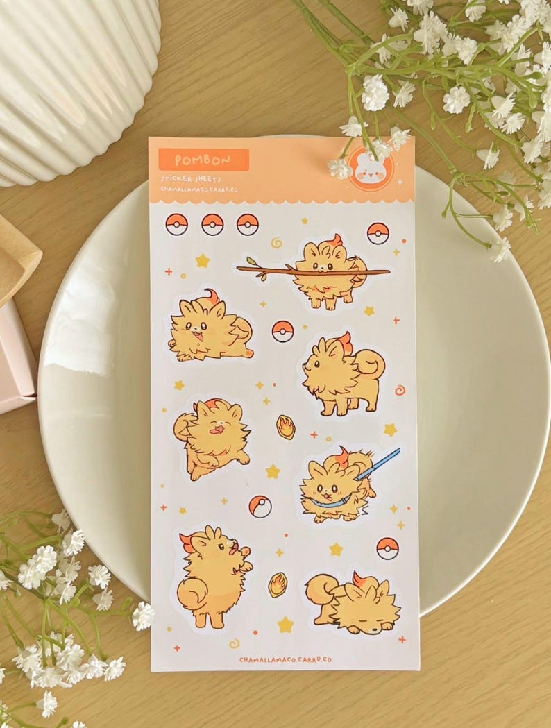 May include: A sticker sheet with cartoon characters in different poses, set against a light orange backdrop. The stickers feature the text "POMBON" and "STICKER SHEETS". The sheet is placed on a white plate, with a floral arrangement.