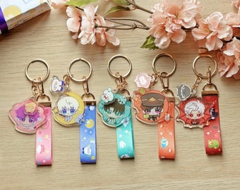 May include: Six colorful keychains with different cartoon characters on them. Each keychain has a gold metal ring and a colorful ribbon.