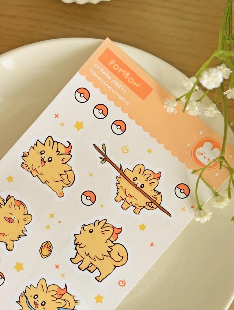 May include: A sticker sheet with cartoon character stickers. The stickers feature an orange, fluffy character with a flame-like mane, stars, and Pok&eacute; Ball designs. The sheet has the word "POMBON" and "STICKER SHEETS" on an orange background.