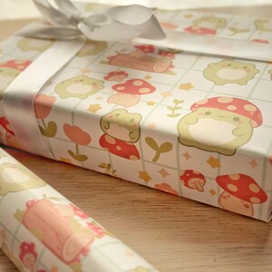 May include: A roll of white wrapping paper with a repeating pattern of green frogs, red mushrooms, and gold stars. The paper is tied with a white ribbon.