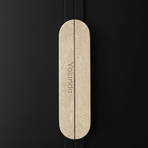 Può includere: Un paio di maniglie per armadi beige con una texture maculata e estremità arrotondate. La parola "Yolanda" è stampata verticalmente su ogni maniglia. Sono montate su un'anta di armadio nera.