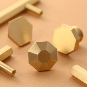 May include: A set of six gold-toned cabinet knobs and pulls. The knobs are octagonal and have a faceted design. The pulls are straight and have a rectangular cross-section.