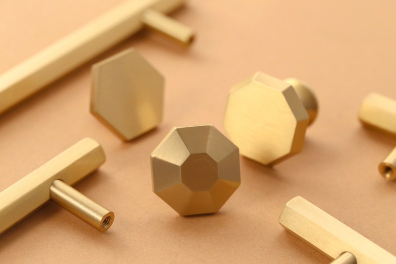 May include: A set of six gold-toned cabinet knobs and pulls. The knobs are octagonal and have a faceted design. The pulls are straight and have a rectangular cross-section.