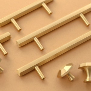 May include: A set of gold-toned cabinet hardware, including pulls and knobs. The pulls are rectangular with a hexagonal shape and the knobs are round with a hexagonal shape.