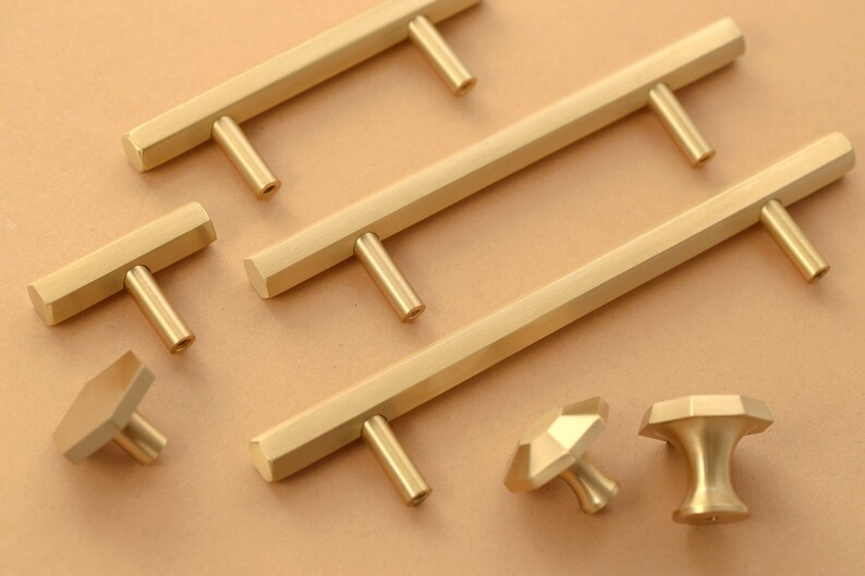 May include: A set of gold-toned cabinet hardware, including pulls and knobs. The pulls are rectangular with a hexagonal shape and the knobs are round with a hexagonal shape.