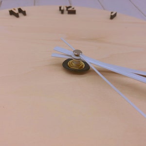 May include: Close-up of a wooden clock face with white hands. The clock face is light brown and has black numbers.