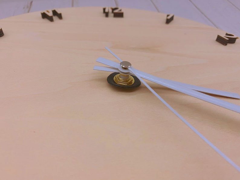 May include: Close-up of a wooden clock face with white hands. The clock face is light brown and has black numbers.