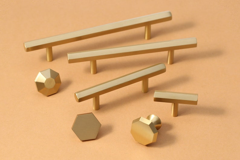May include: A set of six gold-toned cabinet hardware pulls and knobs. The pulls are rectangular with a T-shaped handle. The knobs are octagonal.