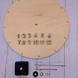 May include: A wooden clock face with numbers 1 through 12, clock hands, and a clock mechanism. The clock face is on a white wooden surface.