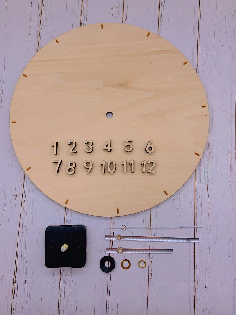 May include: A wooden clock face with numbers 1 through 12, clock hands, and a clock mechanism. The clock face is on a white wooden surface.
