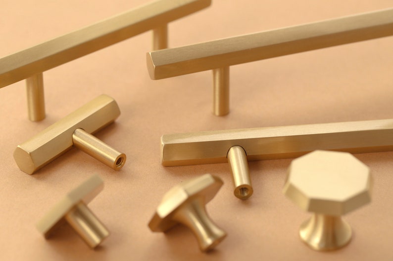 May include: A set of six gold-toned cabinet hardware pulls and knobs. The pulls are rectangular with a hexagonal shape and the knobs are round with a hexagonal shape.