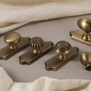 以下が含まれることがあります： アンティーク真鍮のキャビネットノブとプル。ノブは、丸型、リブ型、積層型など、さまざまなデザインがあります。プルは長方形で、装飾的なエッジが付いています。1つのプルには「Yolanda」という名前が刻まれています。