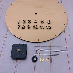 May include: A DIY clock kit with a wooden clock face, black numbers, and a black clock mechanism. The kit also includes three clear clock hands, a black washer, a gold washer, and a gold nut.