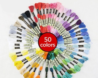 Puede incluir: Una colección de 50 carretes de hilo de bordar dispuestos en círculo, mostrando un arcoíris de colores. Cada carrete tiene una etiqueta negra con texto blanco.