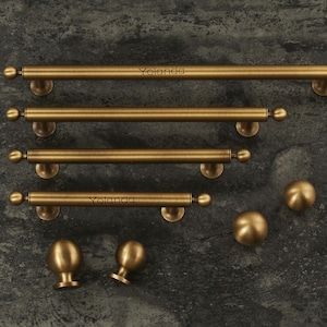 Pode incluir: Uma coleção de ferragens de armário de latão antigo, incluindo várias puxadores de barra e botões redondos. Os puxadores de barra têm um design cilíndrico com extremidades em forma de bola. A palavra "Yolanda" é impressa em dois dos puxadores.