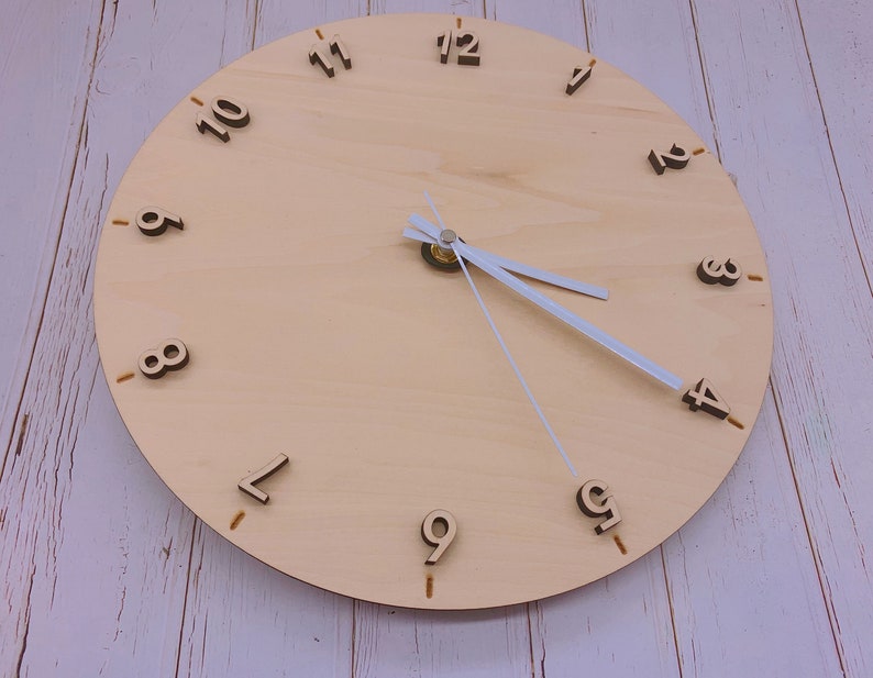 May include: A wooden clock face with black numbers 1 through 12. The clock hands are white and the clock is set to 12:00.