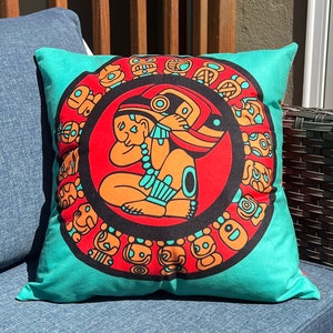 May include: Teal pillow with a red circle featuring a stylized figure and a ring of smaller figures. The figures are in orange, black, and white.