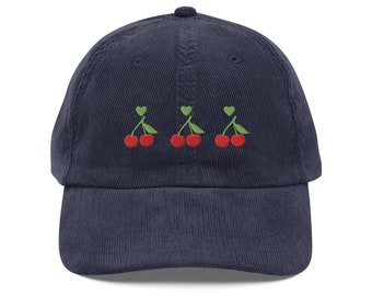 May include: A navy blue corduroy baseball cap with three embroidered red cherries with green stems and leaves.