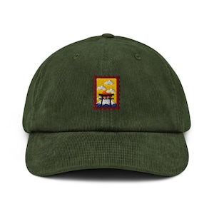 May include: A green corduroy baseball cap with a small embroidered patch. The patch features a Japanese torii gate, clouds, and a sun in a rectangular frame. The cap has a curved brim and a structured crown.