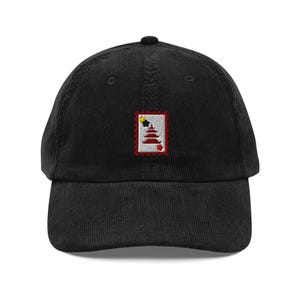 Op de afbeelding: Zwarte corduroy baseballcap met een klein geborduurd ontwerp van een pagode op een postzegel. De pagode heeft rode en witte niveaus, met een geel en zwart ontwerp aan de bovenkant. De cap heeft een gebogen klep en een knoop aan de bovenkant.