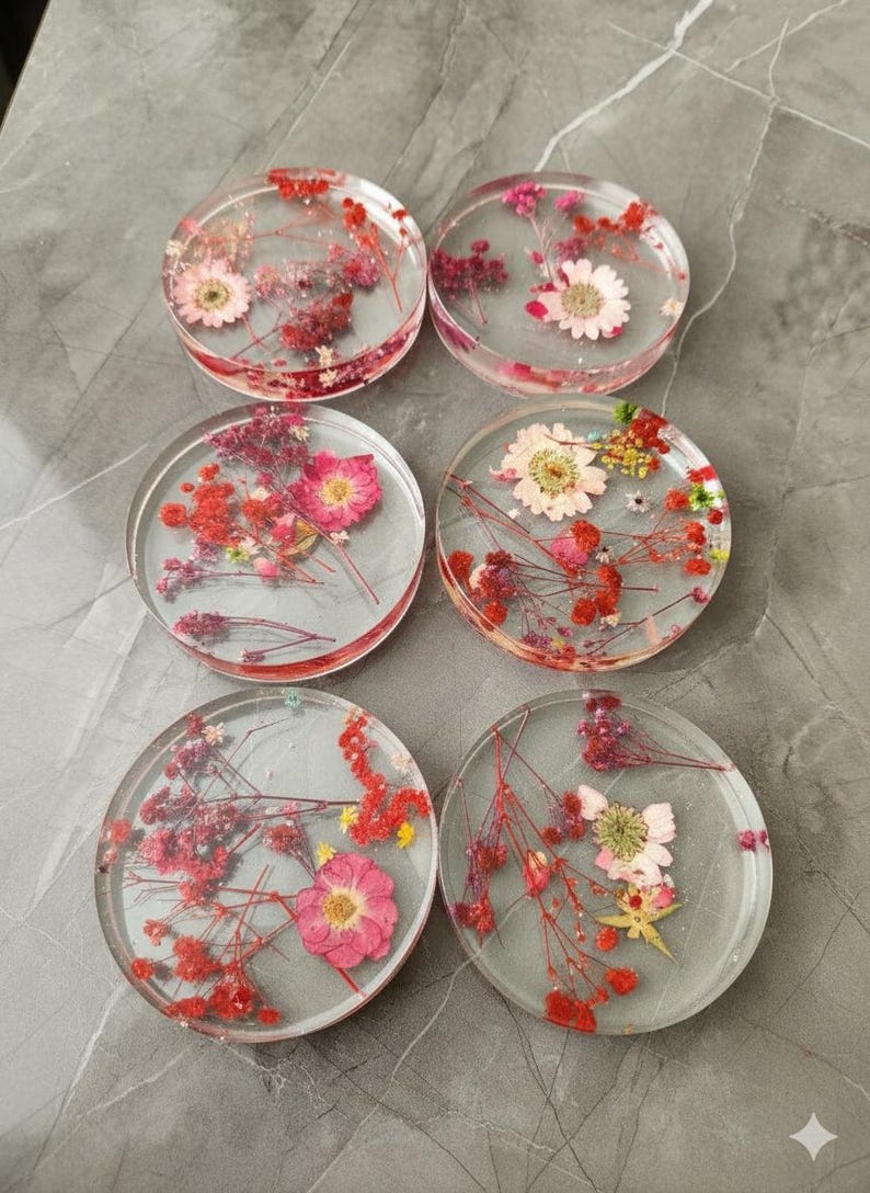 May include: Six clear resin coasters with dried flowers embedded inside. The coasters feature a variety of pink, red, and white flowers and greenery. The coasters are round and appear to be approximately 4 inches in diameter.