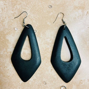 May include: A pair of black wooden earrings with a teardrop shape and a cutout in the center. The earrings have silver hooks.