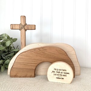 May include: Wooden Easter decor with a cross, a tomb, and a round sign with the text "He is not here. for He is risen, just as He said. Matthew 28:6".