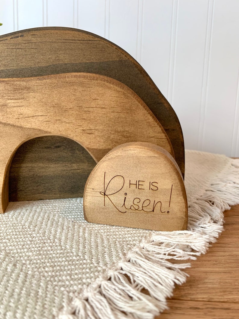May include: Wooden Easter tomb with a brown stain finish. The tomb is made of three pieces that fit together. The top piece has the words "He is Risen!" engraved on it.