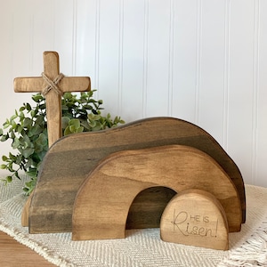May include: Wooden Easter tomb with a cross and a small sign that reads "He is Risen!" The tomb is made of three pieces of wood, each with a different wood grain. The cross is made of a single piece of wood and has a rope tied around it. The sign is made of a single piece of wood and has the words "He is Risen!" engraved on it.