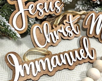 May include: Wooden Christmas decorations with the words "Jesus", "Christ", "Immanuel", and "Savior" written in white cursive lettering.