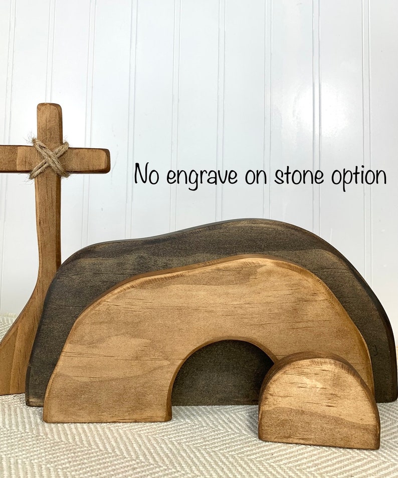 May include: Wooden Easter tomb set with a cross. The tomb is made of three pieces, a large arch, a smaller arch, and a round stone. The cross is tied with twine. "No engrave on stone option" is written on the white wall behind the set.