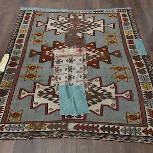 Puede incluir: Una alfombra turca vintage con un patrón geométrico azul, marrón, rojo y amarillo. La alfombra ha sido remendada en varios lugares con diferentes telas.