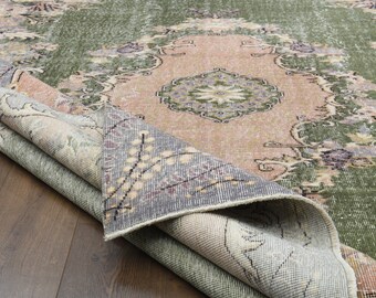 May include: A vintage rug with a green, pink, and gray color scheme. The rug has a floral pattern and is folded in half.