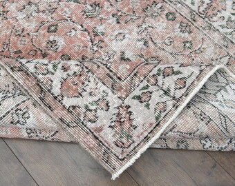 May include: A vintage rug with a floral pattern in shades of pink, white, and black. The rug is folded in half, revealing the intricate details of the design.