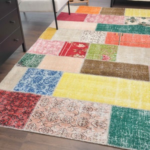 K&ouml;nnte beinhalten: Ein farbenfroher Patchwork-Teppich mit einer Vielzahl rechteckiger Formen in Rot-, Gelb-, Gr&uuml;n-, Blau- und Beiget&ouml;nen. Der Teppich hat ein abgenutztes, Vintage-Aussehen, das seinen einzigartigen Charakter unterstreicht. Der Teppich liegt auf einem Holzboden.