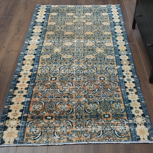 May include: A vintage rug with a blue, orange, and cream floral pattern. The rug has a fringed edge and is perfect for adding a touch of bohemian style to any room.