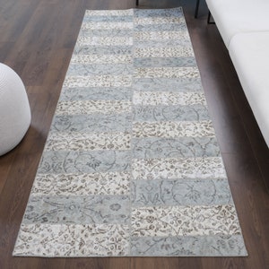 May include: A light blue and cream runner rug with a patchwork design. The rug has a floral pattern and is made of a soft, durable material.