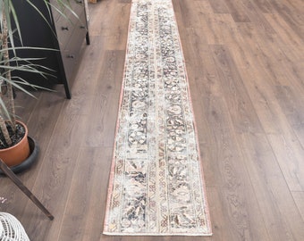 May include: A vintage runner rug with a faded floral pattern in shades of cream, brown, and black. The rug has a distressed look and is perfect for adding a touch of bohemian style to your home.