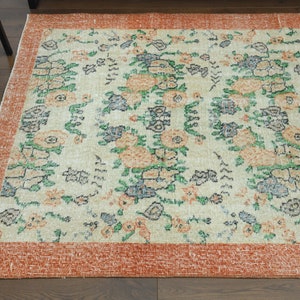 K&ouml;nnte beinhalten: Ein Vintage-Teppich mit einem floralen Muster in Orange-, Gr&uuml;n- und Blaut&ouml;nen auf cremefarbenem Hintergrund. Der Teppich hat einen rostfarbenen Rand.