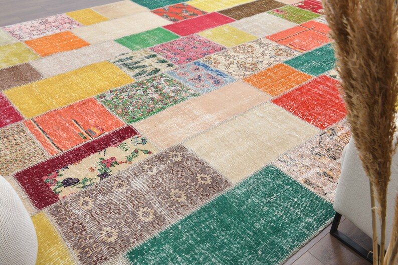 K&ouml;nnte beinhalten: Ein farbenfroher Patchwork-Teppich mit einer Vielzahl von geometrischen Formen und Mustern. Der Teppich weist eine Mischung aus Farben auf, darunter Rot, Gr&uuml;n, Gelb, Orange und Beige. Der Teppich besteht aus mehreren zusammengen&auml;hten Stoffst&uuml;cken.