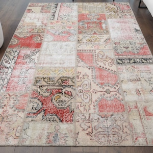 Puede incluir: Una alfombra de patchwork con fondo crema y patrones rojos, rosas y negros. La alfombra está hecha de diferentes piezas de tela cosidas juntas.