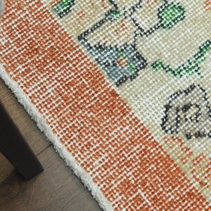 K&ouml;nnte beinhalten: Nahaufnahme eines gewebten Teppichs mit wei&szlig;em Hintergrund und orangefarbenen, gr&uuml;nen und schwarzen Blumenmustern. Der Teppich hat einen Fransenrand.
