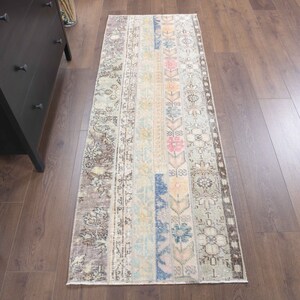 Op de afbeelding: Een vintage loper met een vervaagd bloemenpatroon in roze, blauwe en beige tinten. De loper heeft een verweerde uitstraling en een bruine rand.