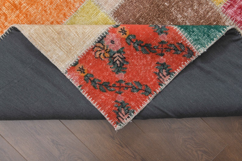 K&ouml;nnte beinhalten: Ein mehrfarbiger Patchwork-Teppich mit einer Vielzahl von Mustern. Der Teppich hat einen zentralen Bereich mit rotem Hintergrund und floralen Designs. Weitere Bereiche sind orange, beige, gelb, gr&uuml;n und braun. Der Teppich liegt auf einer dunkelgrauen Oberfl&auml;che.