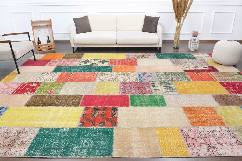 K&ouml;nnte beinhalten: Ein gro&szlig;er, rechteckiger Patchwork-Teppich mit einer lebendigen Mischung aus Farben und Mustern. Der Teppich weist eine Vielzahl geometrischer Formen in Rot-, Gelb-, Gr&uuml;n- und Beiget&ouml;nen auf und erzeugt eine optisch ansprechende und strukturierte Oberfl&auml;che.