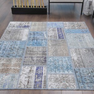 Könnte beinhalten: Ein Patchwork-Teppich in Blau- und Grautönen. Der Teppich besteht aus verschiedenen Stoffstücken, die zusammengenäht wurden und ein einzigartiges und interessantes Design ergeben.