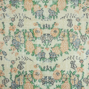 K&ouml;nnte beinhalten: Ein Vintage-Teppich mit cremefarbenem Hintergrund und einem floralen Muster in Orange-, Gr&uuml;n- und Blaut&ouml;nen. Der Teppich hat einen orangefarbenen Rand.